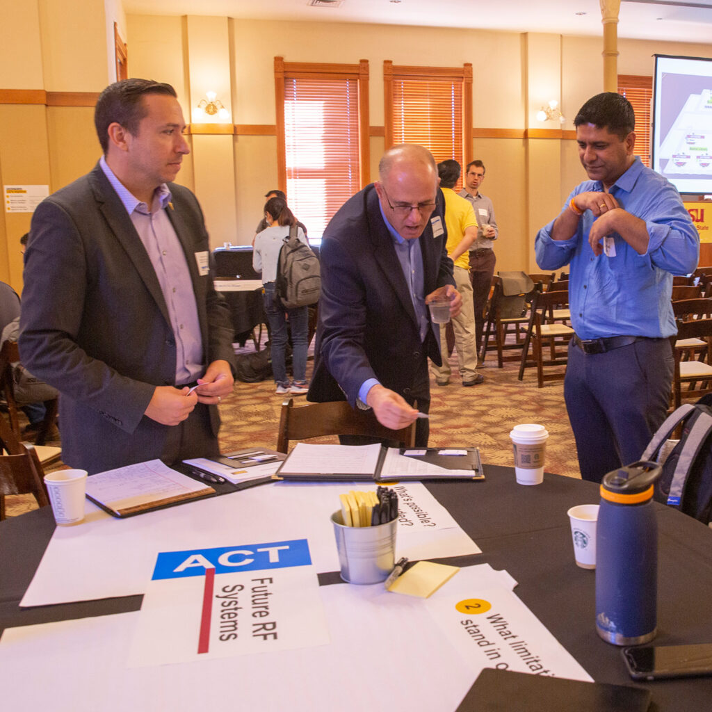 Participants at the 2022 Proposers Day event gather around a table full of sticky notes and poster boards. 