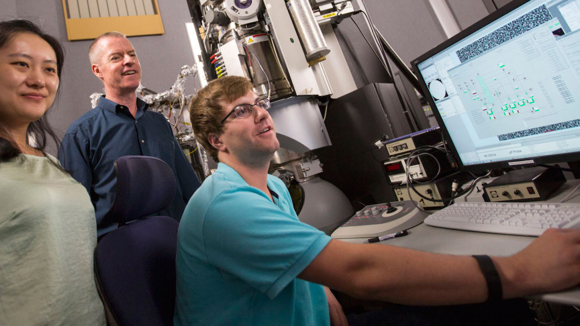 Peter Crozier and two of his graduate students sit at a computer in his lab.
