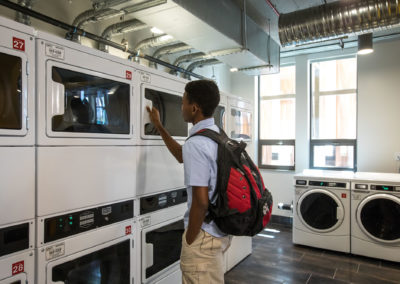A young man student is looking at a dryer in the laundry facilities.