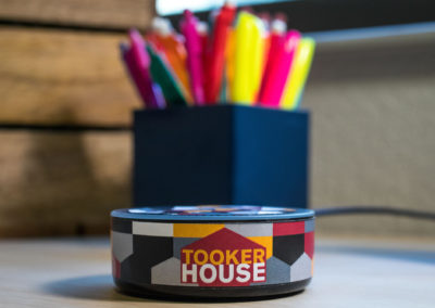 A Tooker House-branded Echo Dot (TM) sits on a desk in front of a box of pencils and highlighters.