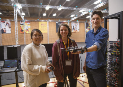Three students standing holding devices in view of the ASU Drone Studio's servers