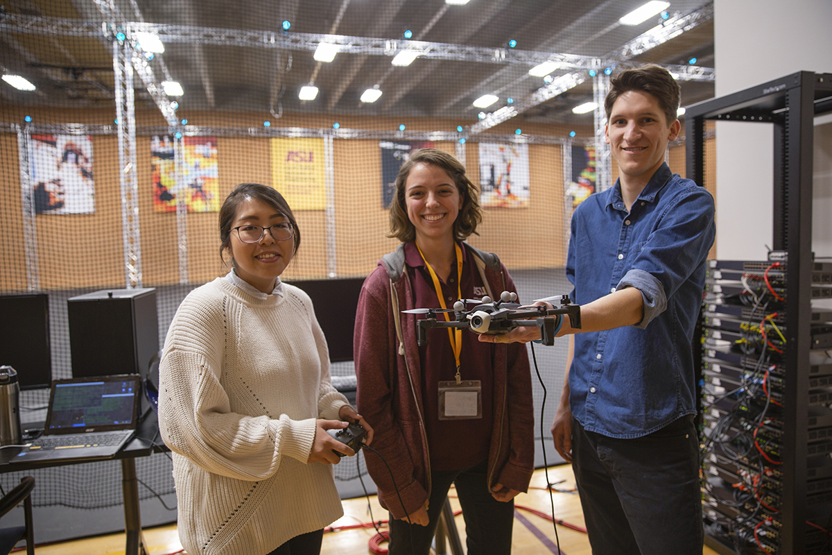 Three students standing holding devices in view of the ASU Drone Studio's servers