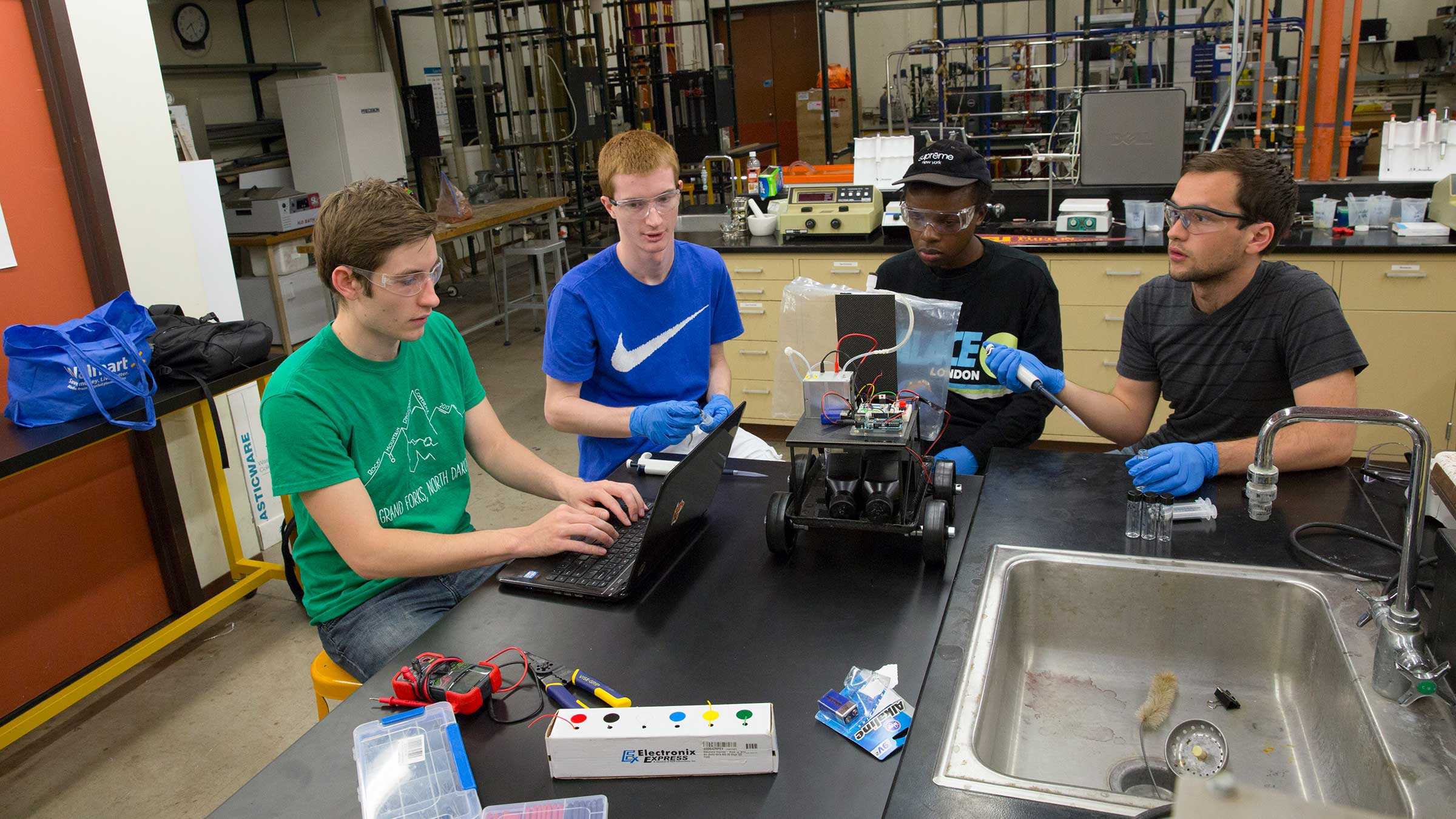 Four male engineering students students work at a lab table on a project