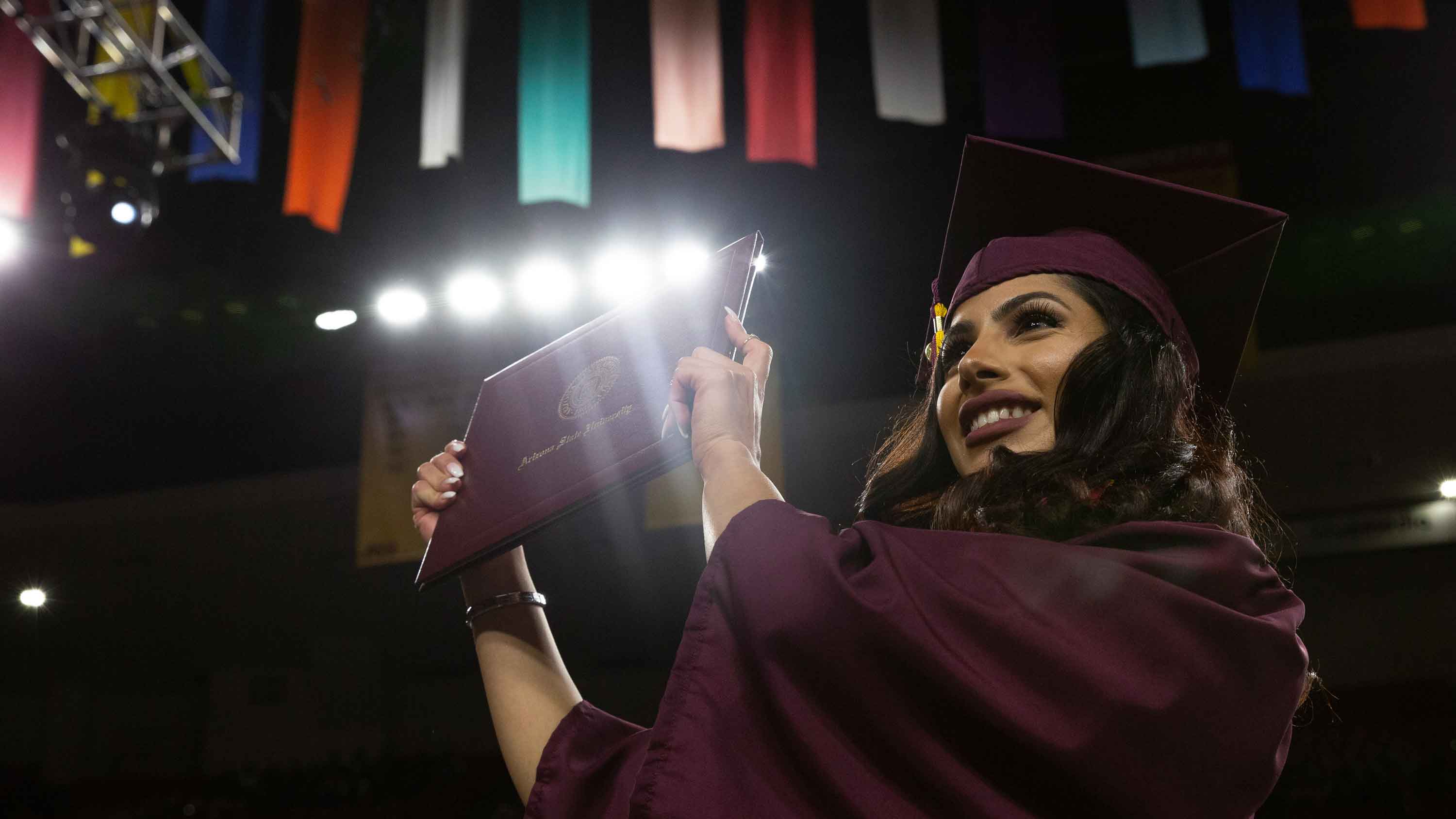 A graduate holds up her diploma, smiling, as she crosses the stage at the Fulton Schools Convocation