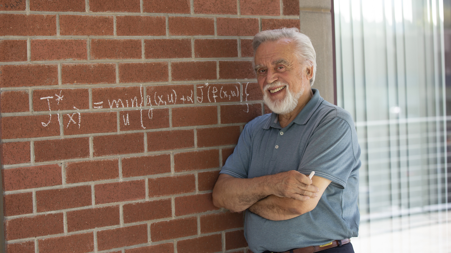 Dimitri Bertsekas stands in front of an ASU building on which he's written a mathematical equation in chalk