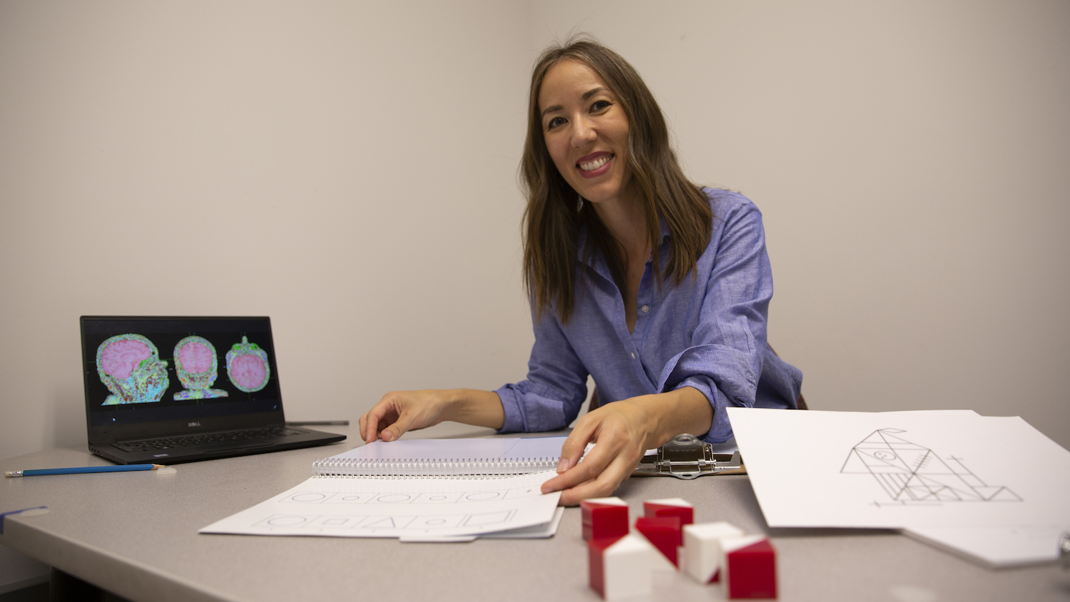 Sydney Schaefer sits at her desk displaying some of the low-cost cognitive tests (papers with drawings) she uses in her research
