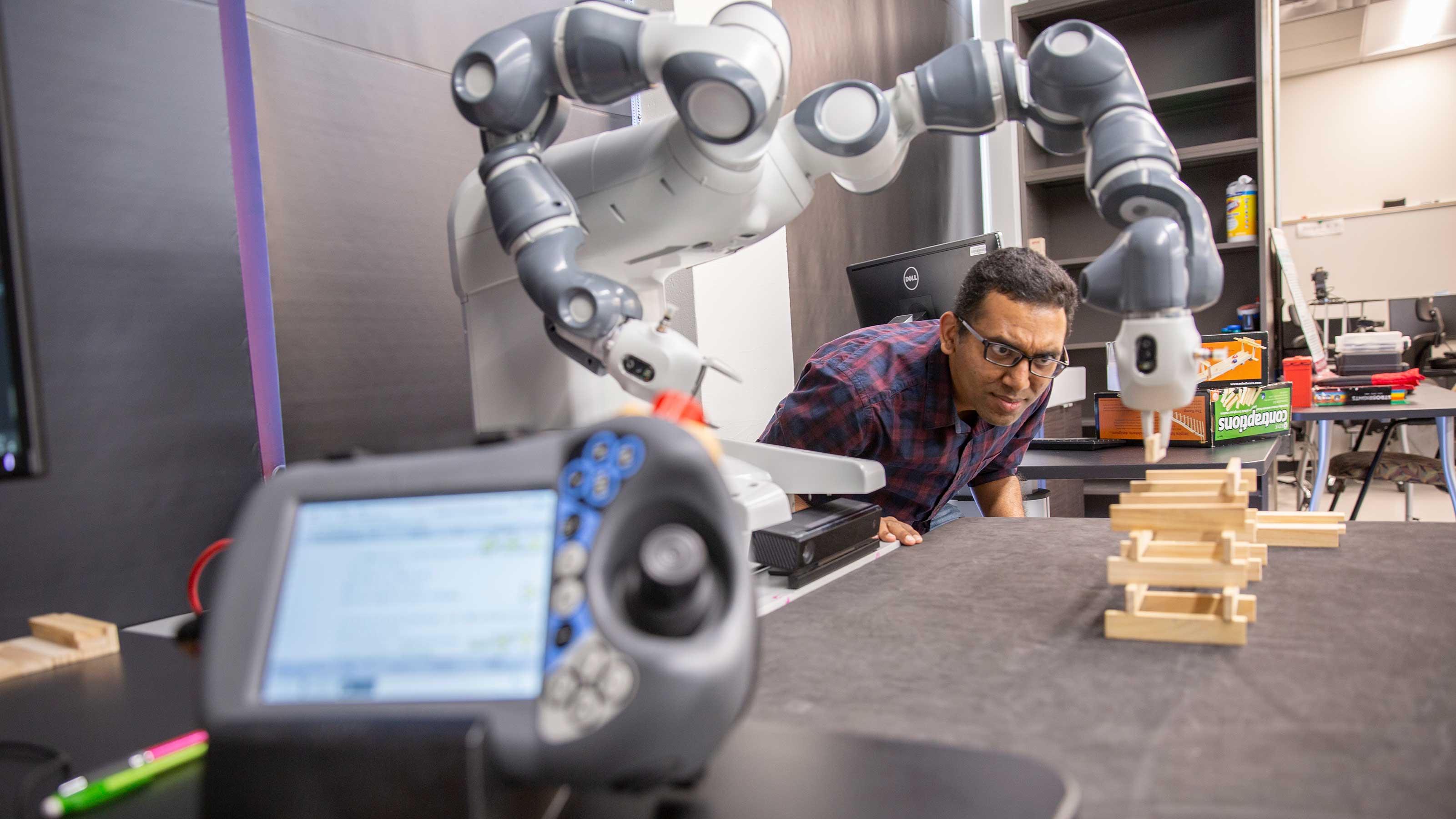 A member of Siddharth Srivastava's lab looks on as an autonomous robot builds a wood block tower