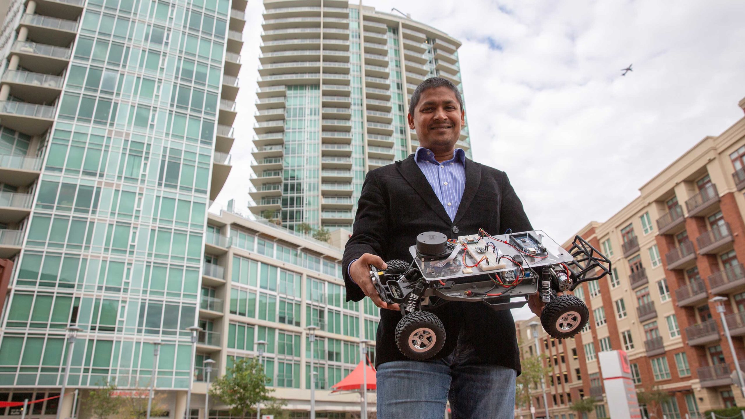 Aviral Shrivastava stands outside in downtown Tempe Arizona holding his small autonomous vehicle
