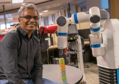 Rao Kambhampati poses for the camera in his lab next to a robot that has just stacked some alphabet blocks