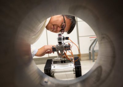 Yongming Liu looks closely at a robot on rotating, tank-like tread that he is preparing to send down a pipeline