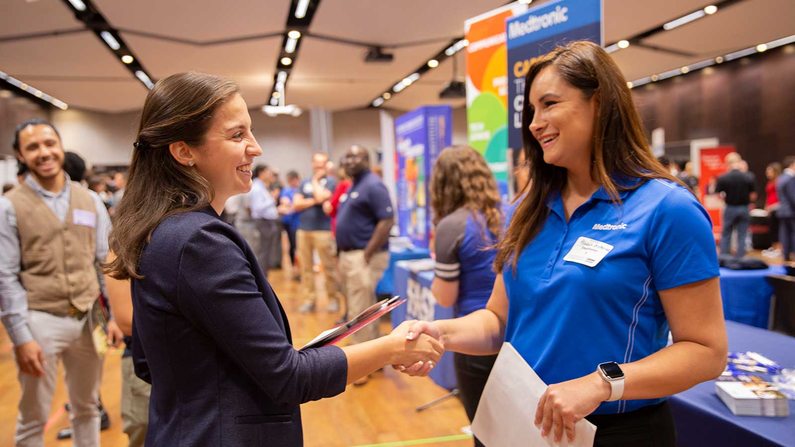 An employer and student shake hands and smile amidst the Fulton Schools Career Fair