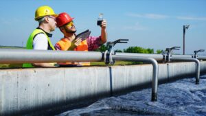 Two workers collect a water sample from a wastewater treatment plant