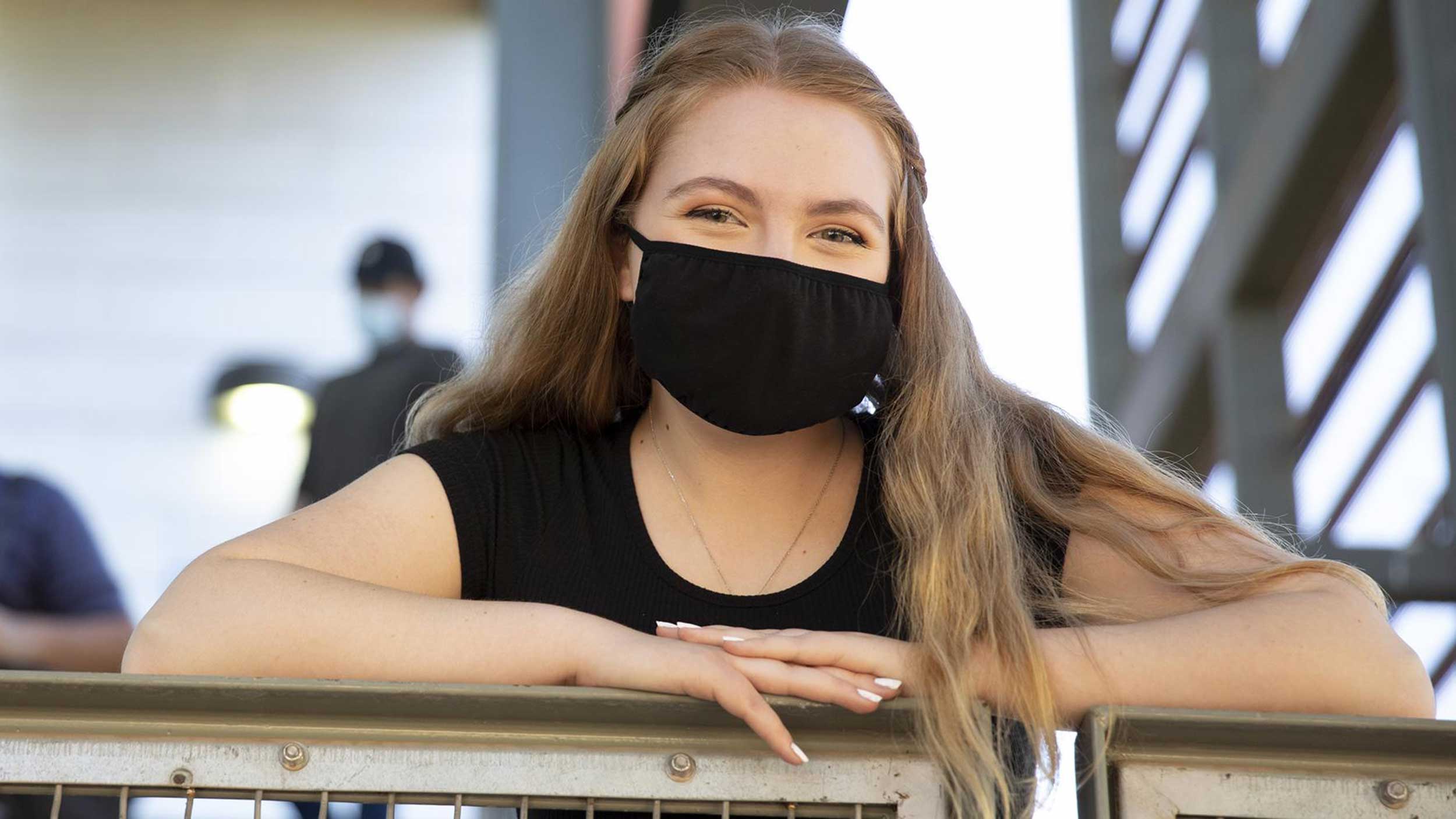 An ASU student smiles for the camera wearing a black face mask