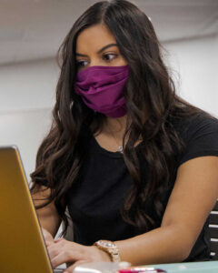A woman wearing a mask works at her laptop