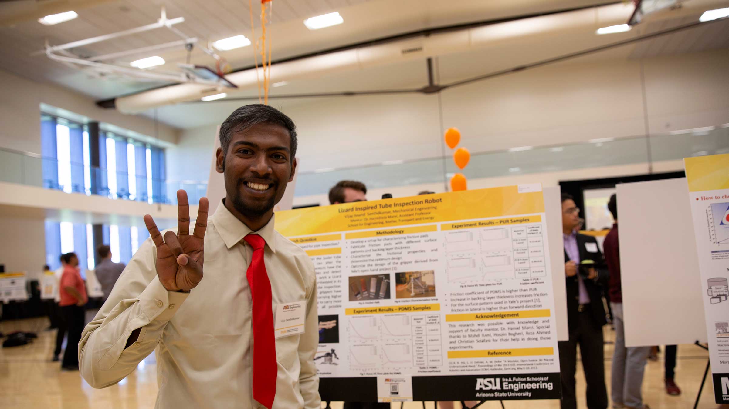 An international student from India stands by his research poster at FURI