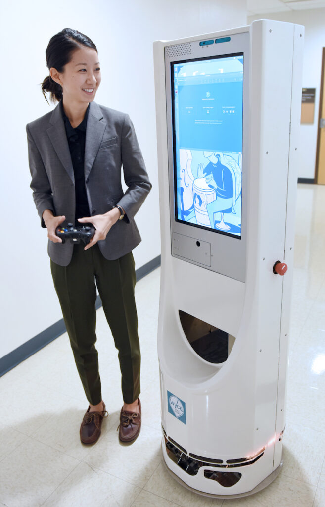 Erin Chiou walks with a mobile robot prototype that looks like a large screen on a circular mobile base