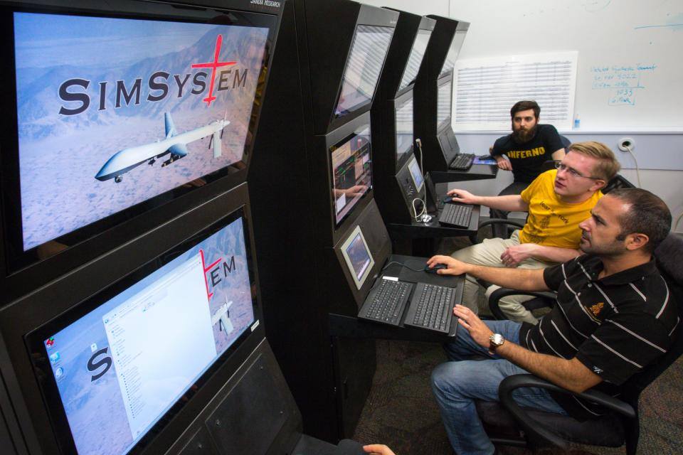 Three students work at simulation stations testing the interactions between people and unmanned aerial systems controls