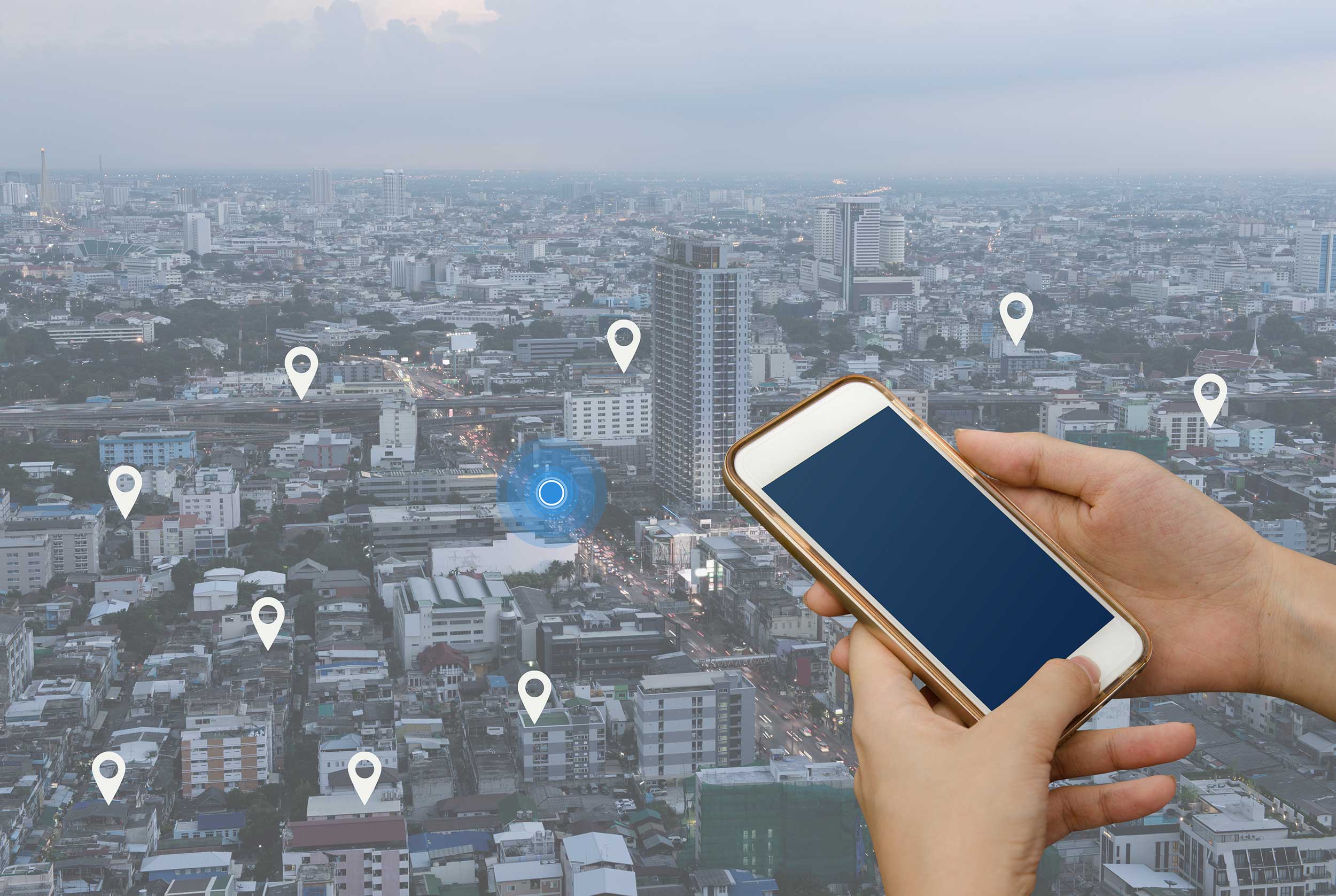 Stylized stock image of a person holding a cell phone against a cityscape that is sprinkled with map pinpoints