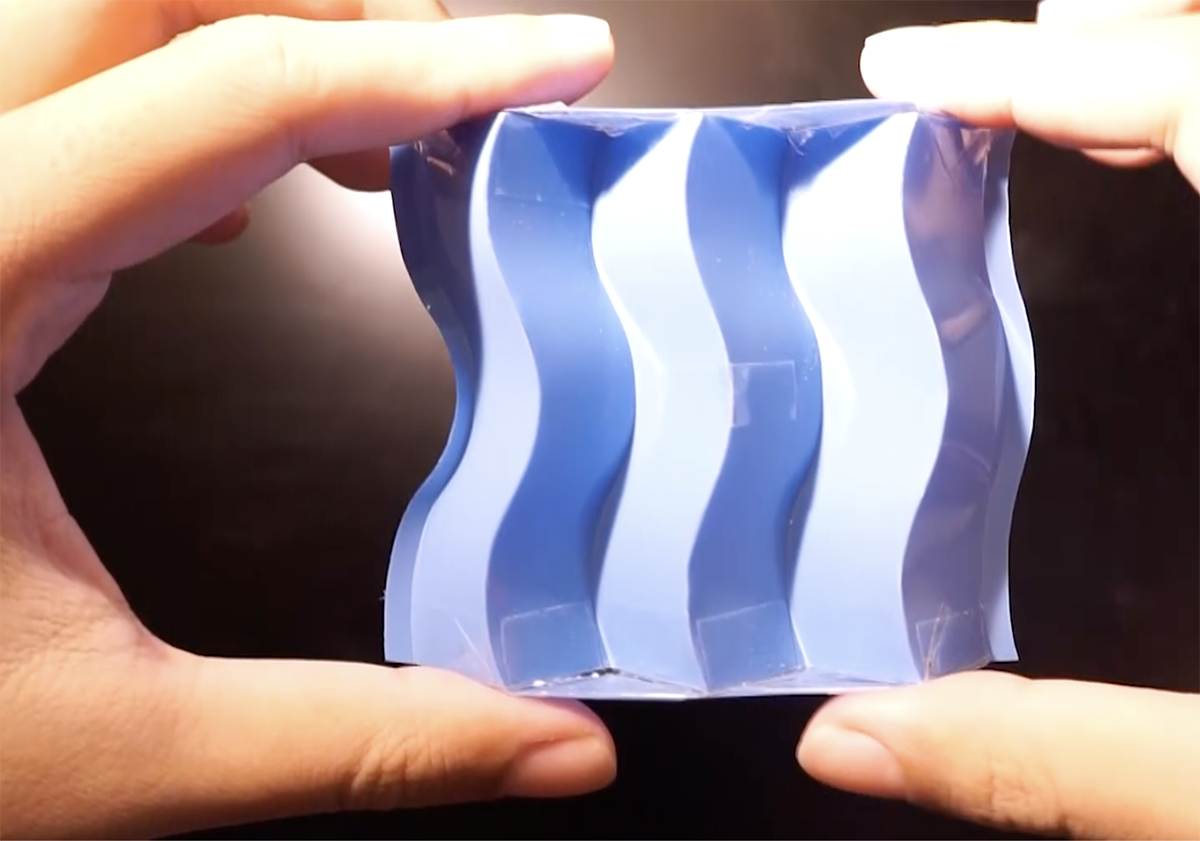 A person holds a curved orgami example that looks like blue plastic with curvy, wave-like "pleats"