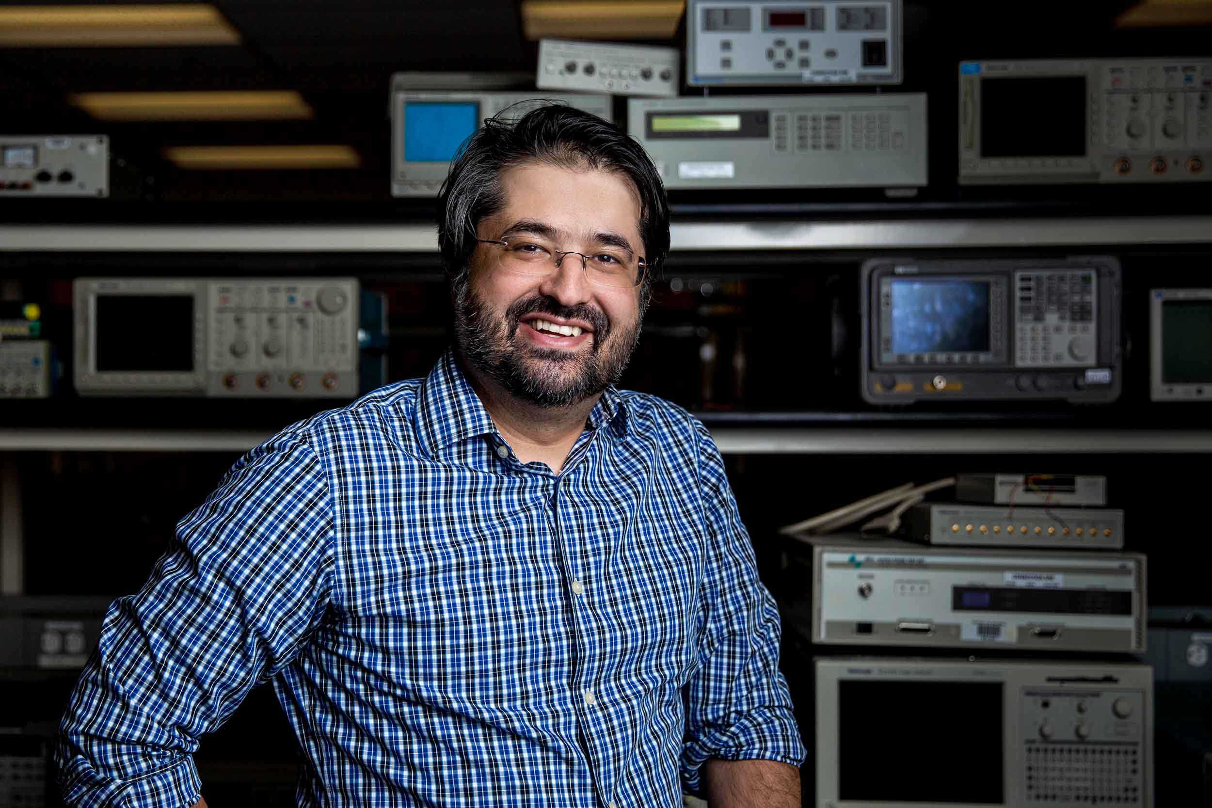 Mohammadreza Imani stands smiling warmly in his lab surrounded by electronics