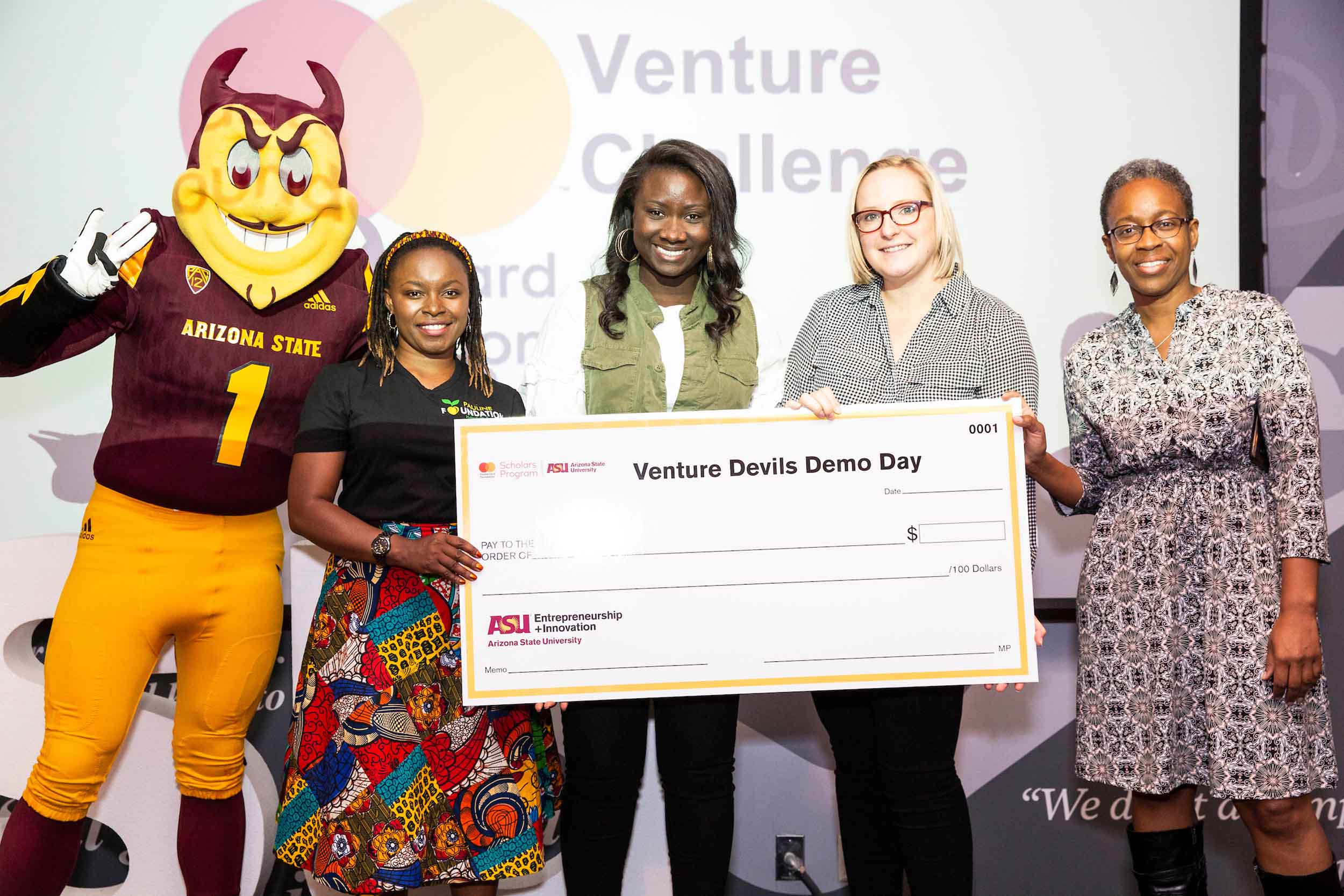 Four women and ASU's mascot, Sparky, stand together holding a gigantic check for Venture Devils Demo Day in April of 2019