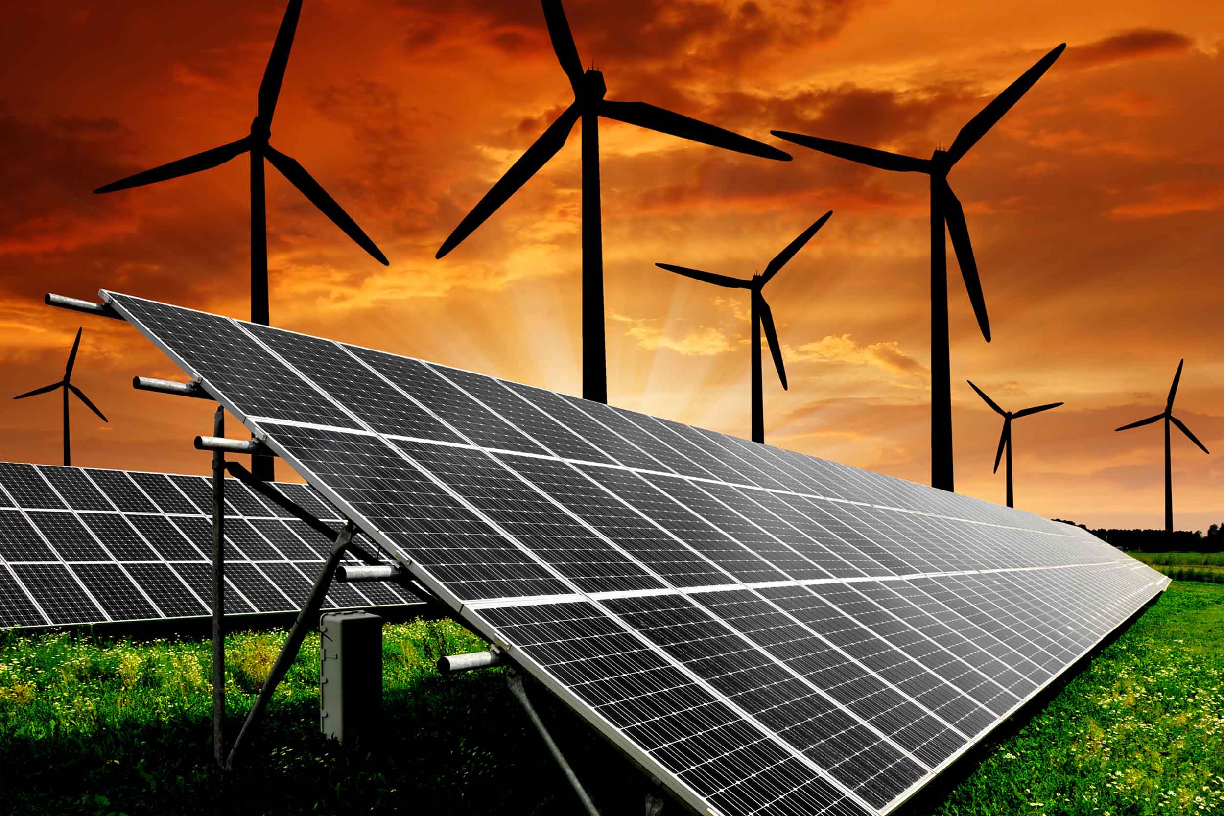 Stock image of a green, grassy field with solar panel arrays, windmills and a rich red sunset