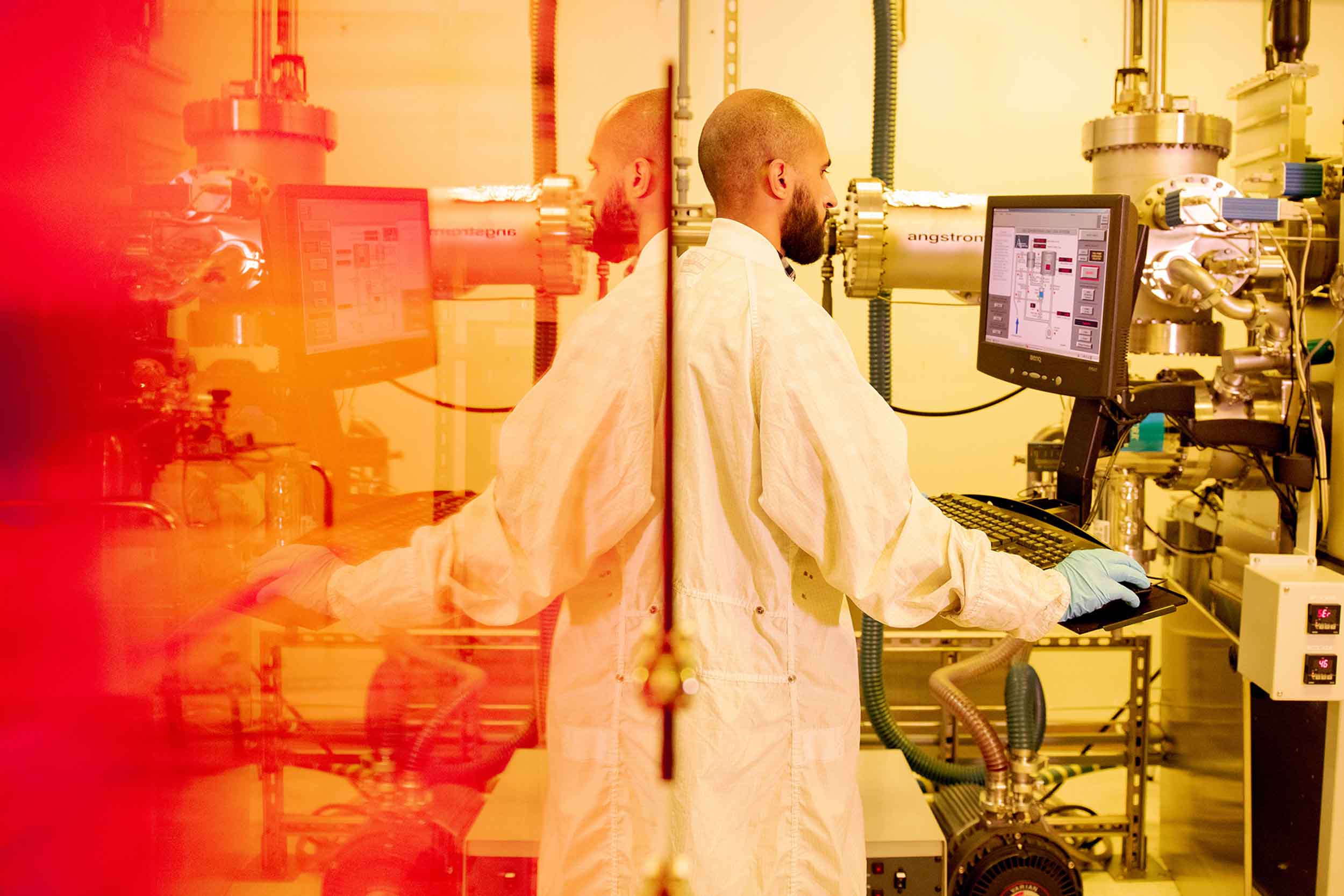 ASU Researcher Wahab Alasfour stands at a computer in his lab wearing a lab coat, working on his semiconductor research