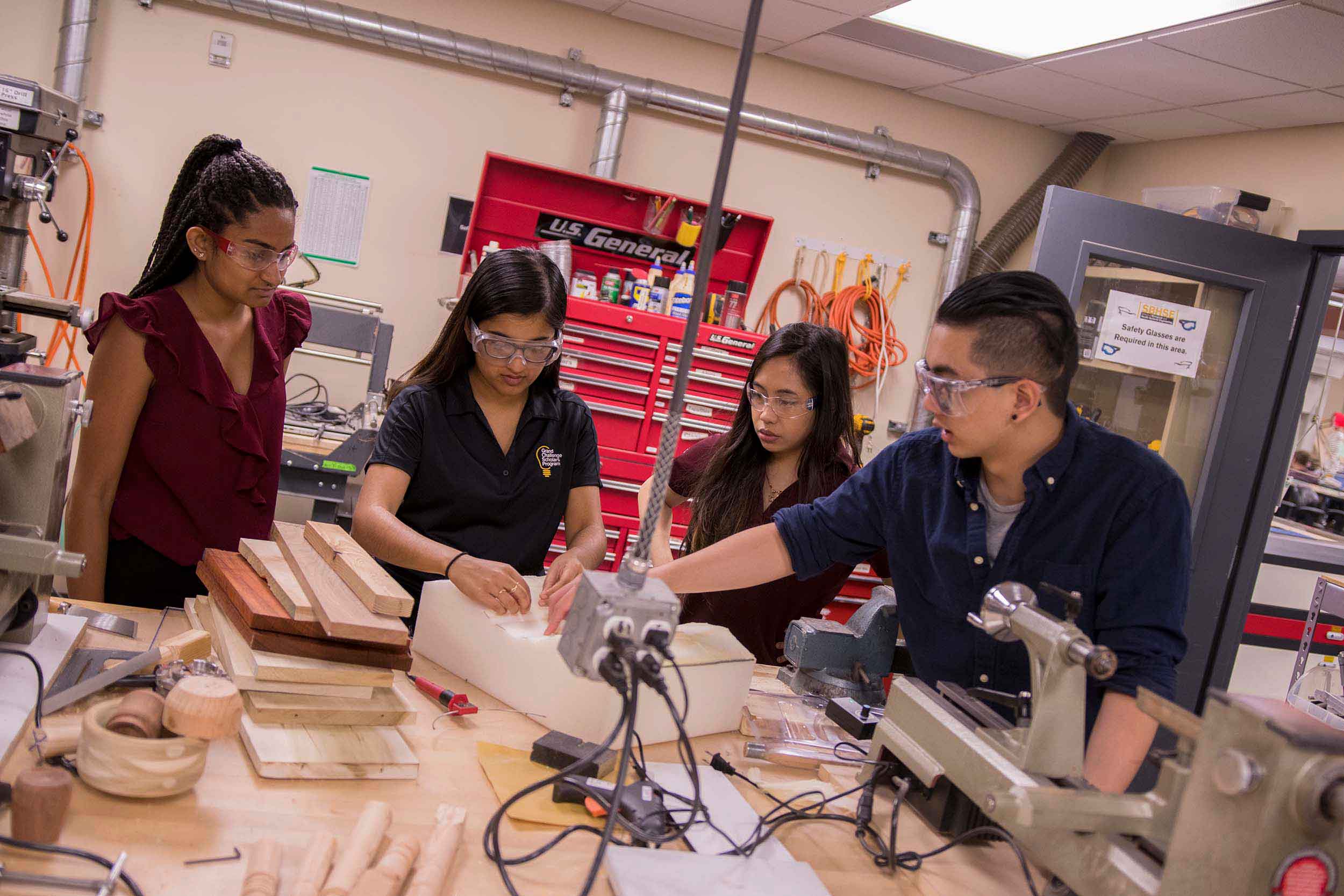 4 undergraduate students work in a research lab/workshop, surrounded by building tools and materials, creating a prototype