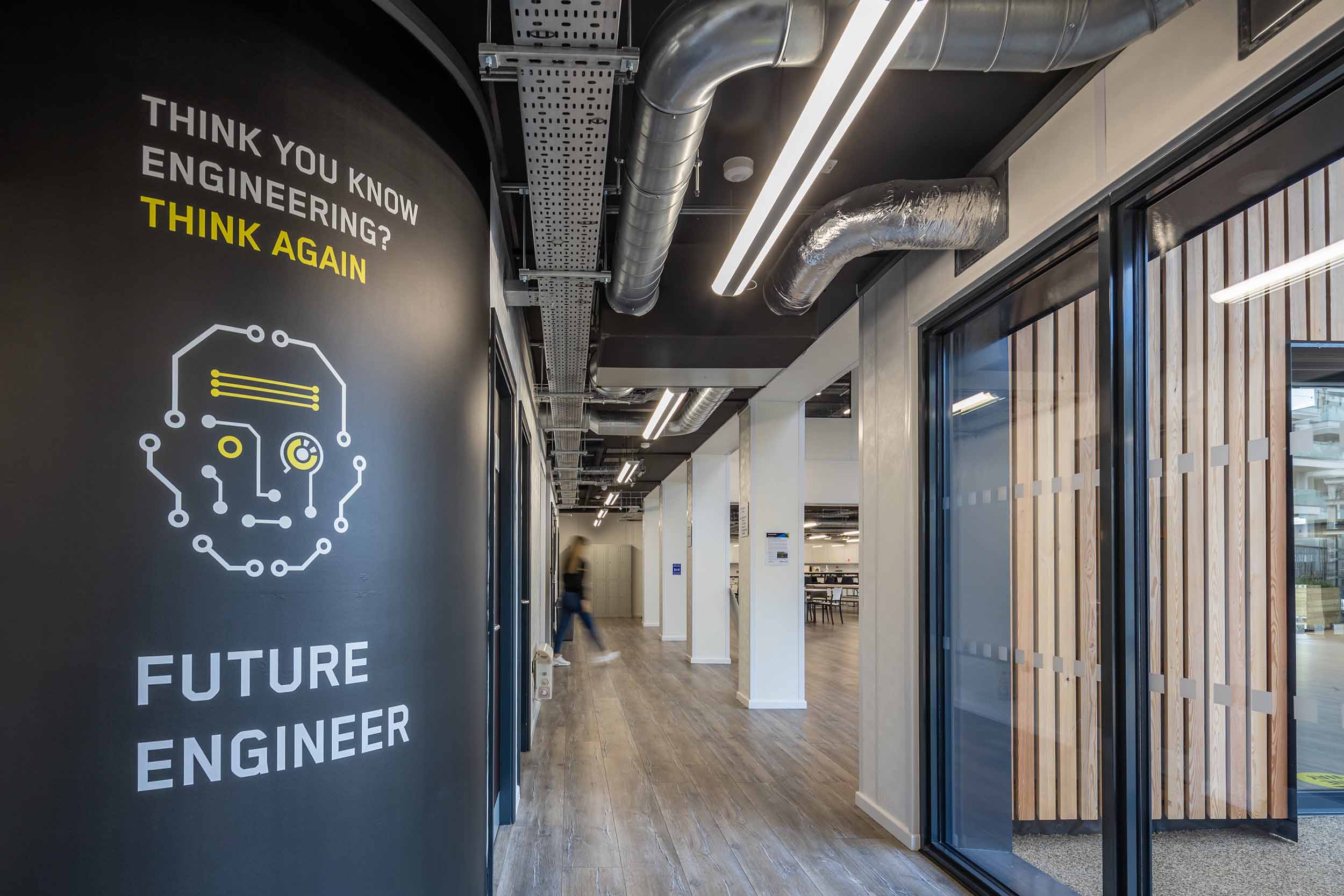 A view of a hallway within the TEDI-London building with a wall containing the words "Think you know Engineering? Think Again. Future Engineer" and a robotic face graphic