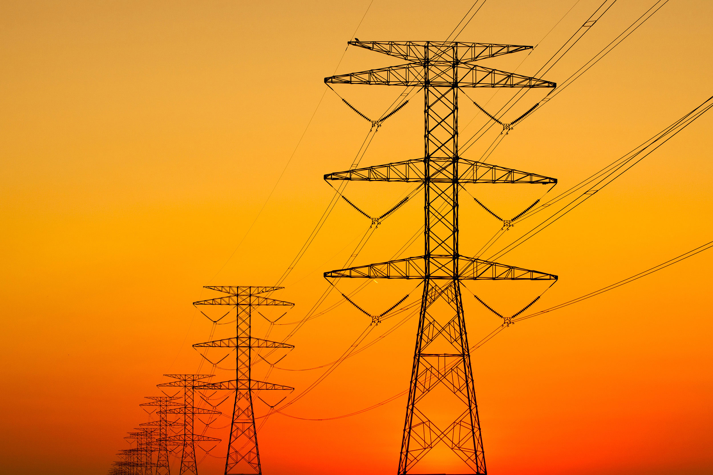 A large string of powerlines set against a brilliant orange sunset