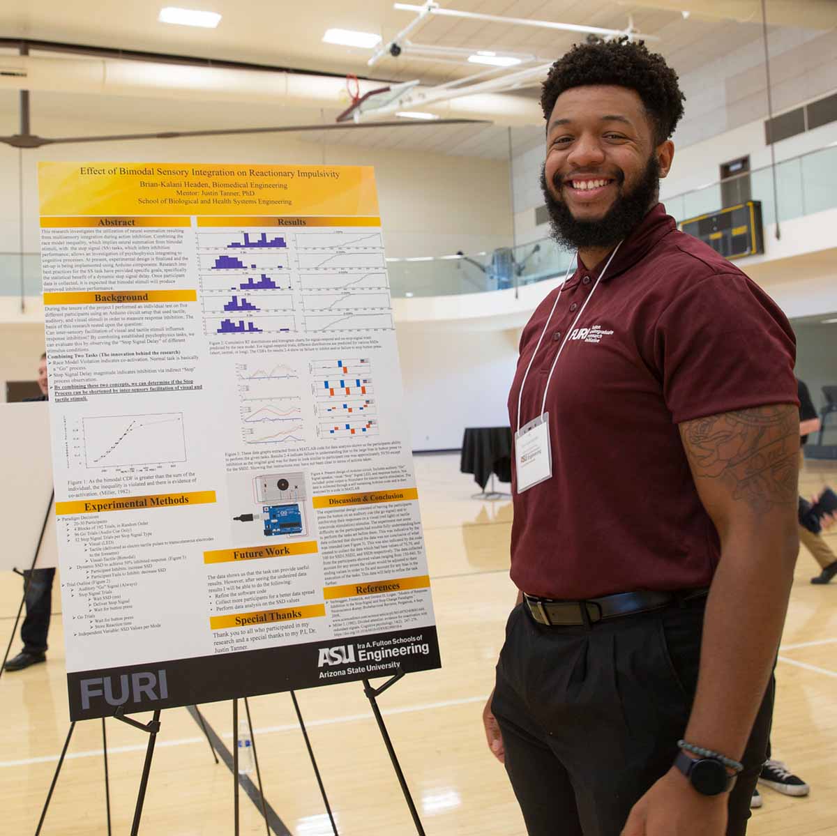 A student stands by his poster, smiling for the camera, at the FURI symposium