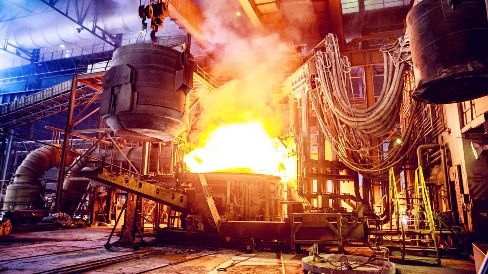 Stock image, possibly AI, of the innards of a hot, old fashioned looking factory with a huge fire burning in the center.