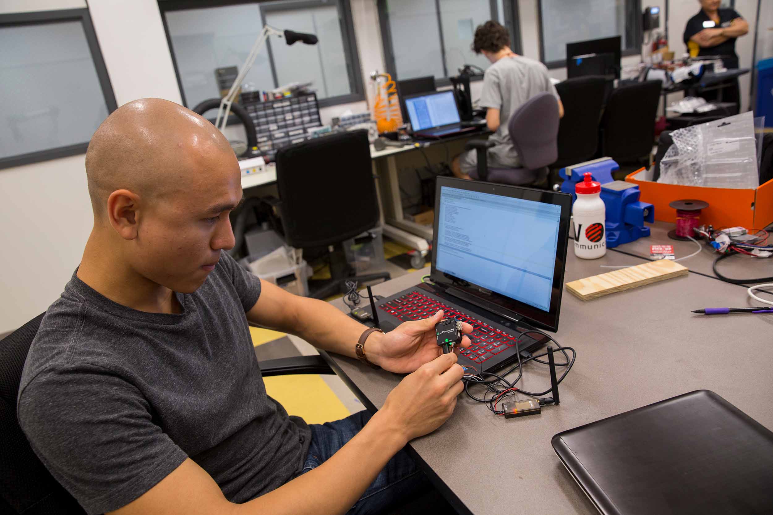 A student works on an electronic device at a laptop in a robotics research lab