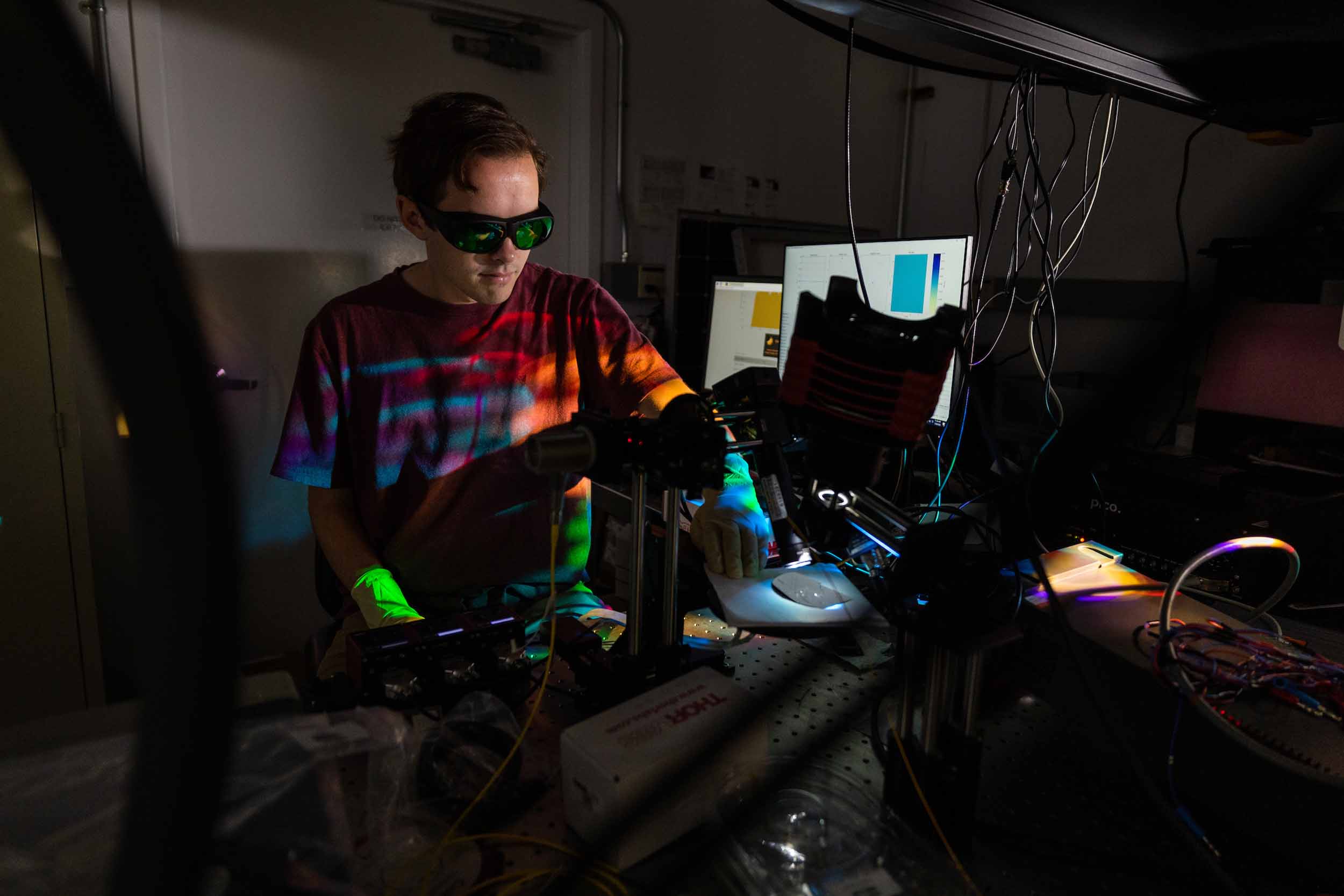 A student works in a dark laboratory at a lab bench using a laser