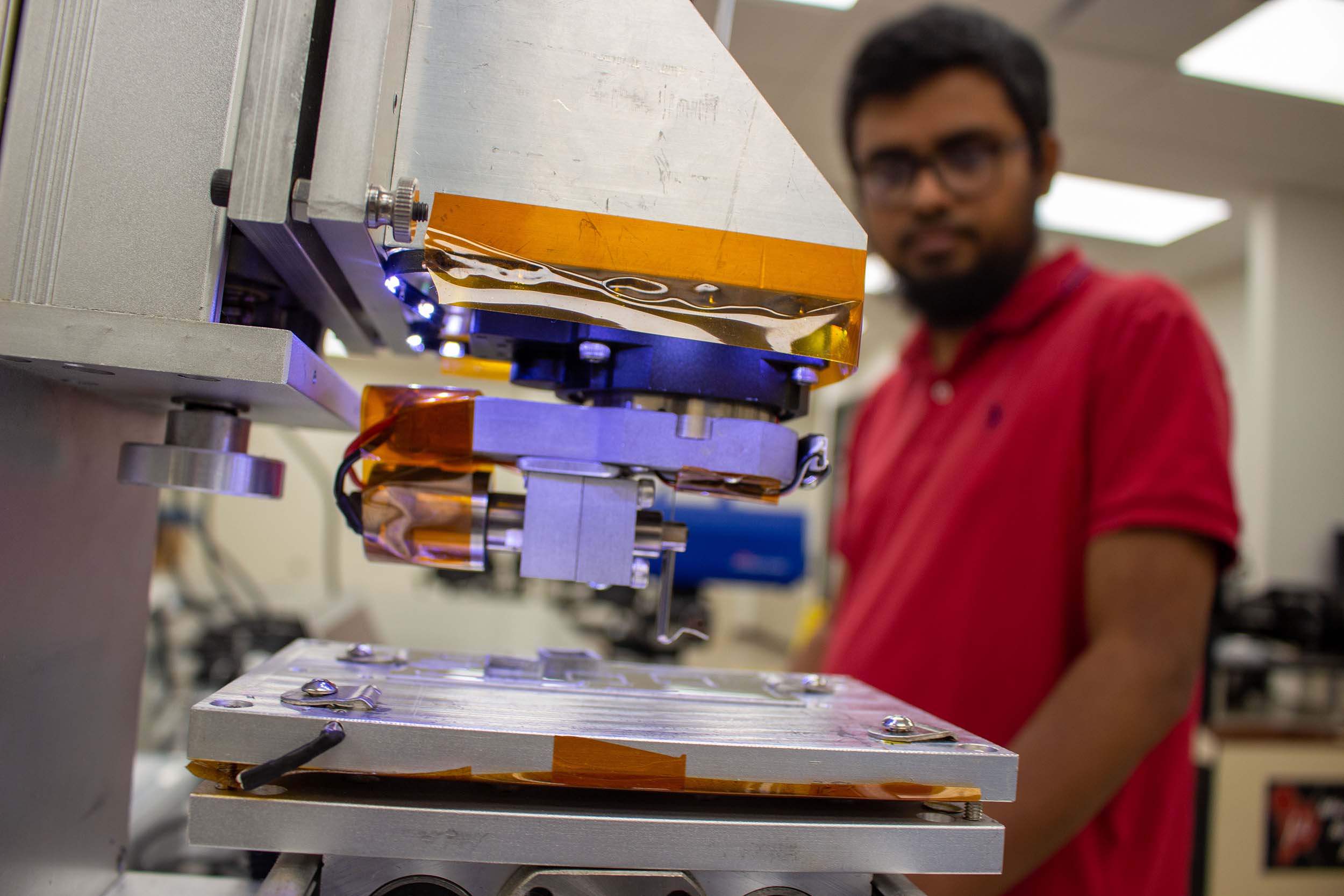A man in an engineering lab looks on as an advanced 3D printer begins building an object