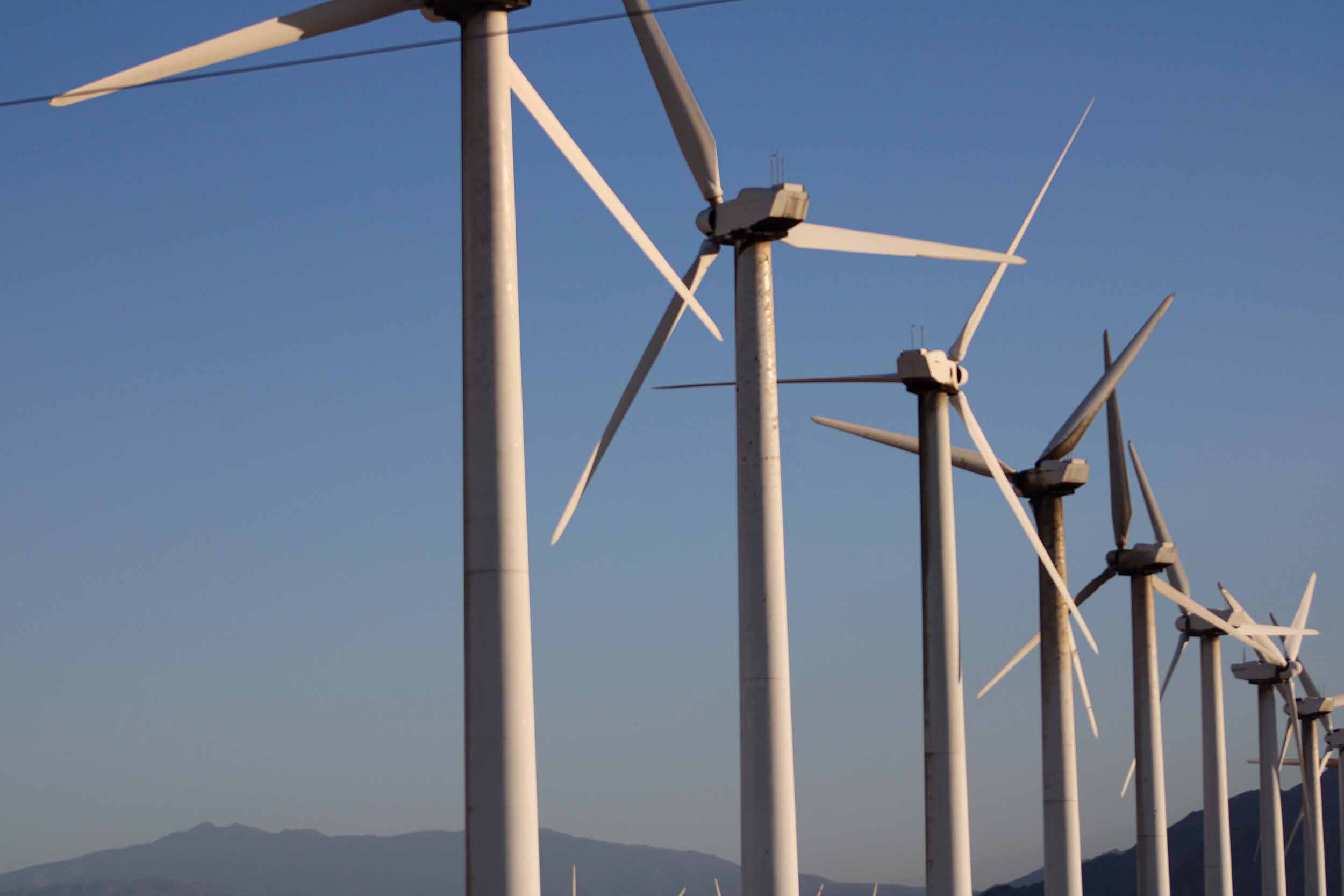 row of windmills on a wind farm against a blue sky with mountains in the background