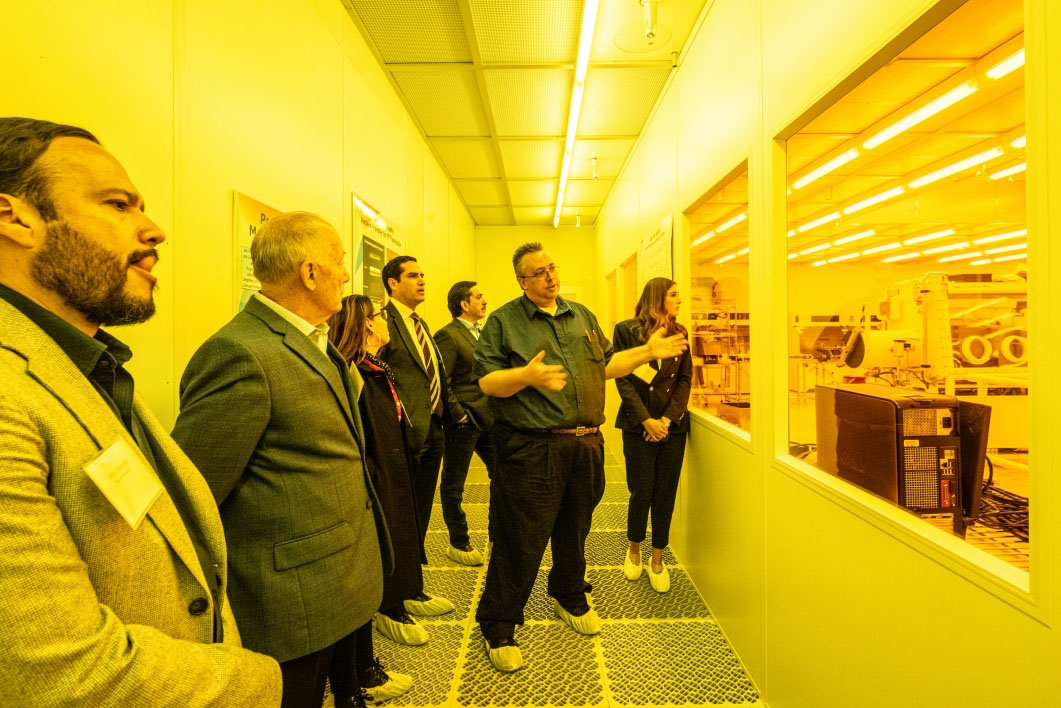 Under bright yellow lights, Research scientist Michael Marrs speaks to a small crowd of people looking through windows at the MacroTechnology Works facility at ASU Research Park