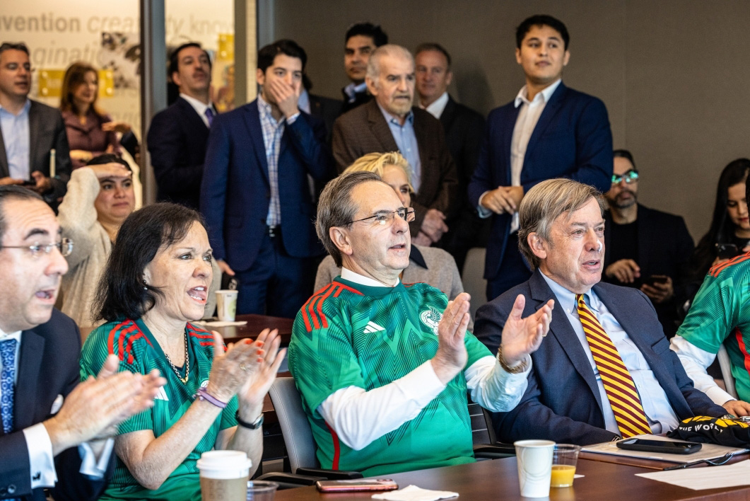 A small crowd of people, including Ambassador Esteban Moctezuma Barragán and Michael Crow, clap while they watch the Mexico vs. Poland World Cup game.