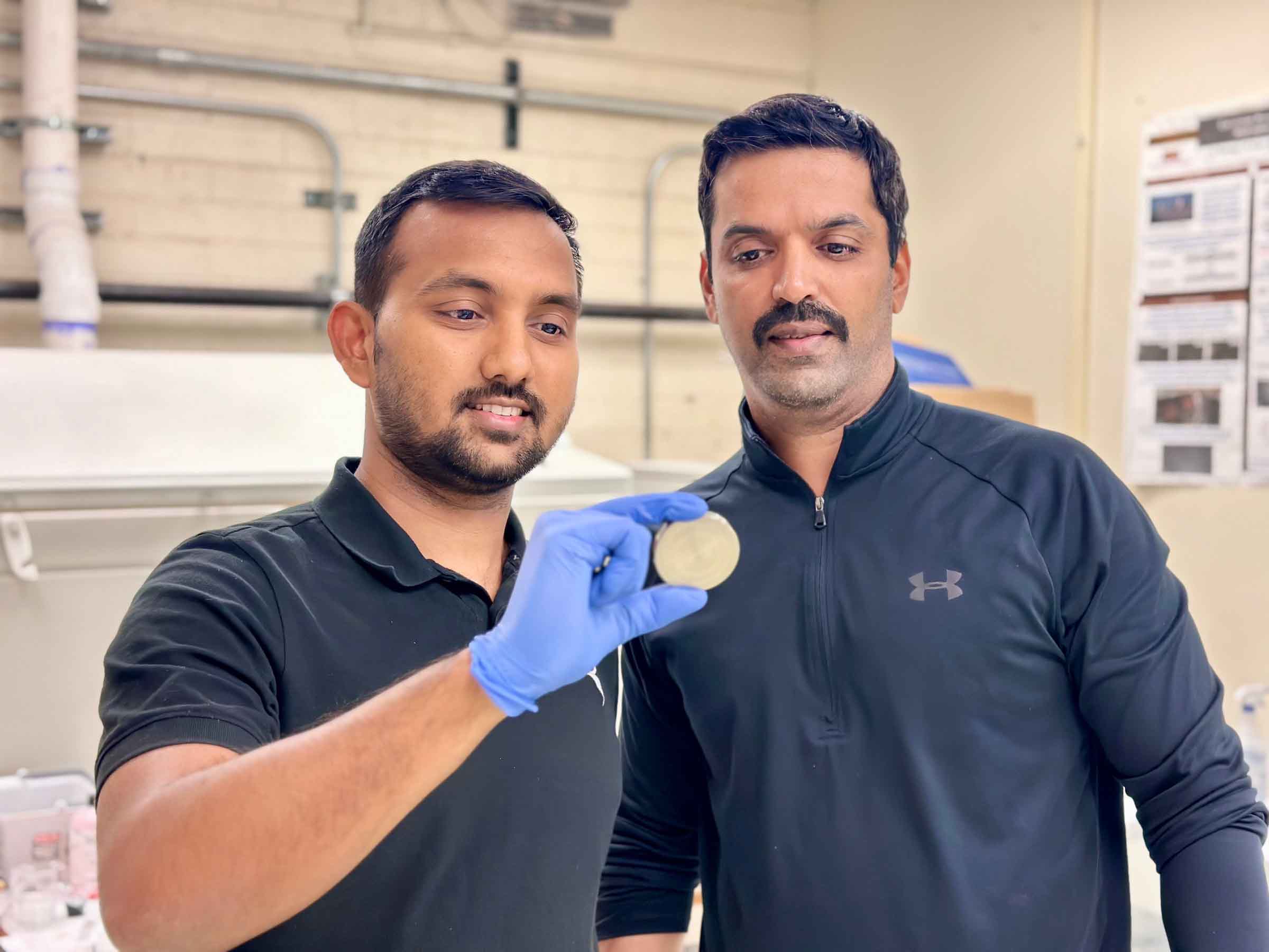 Kiran Solanki and Vikrant Beura stand together in Solanki's lab, looking at a metal disc