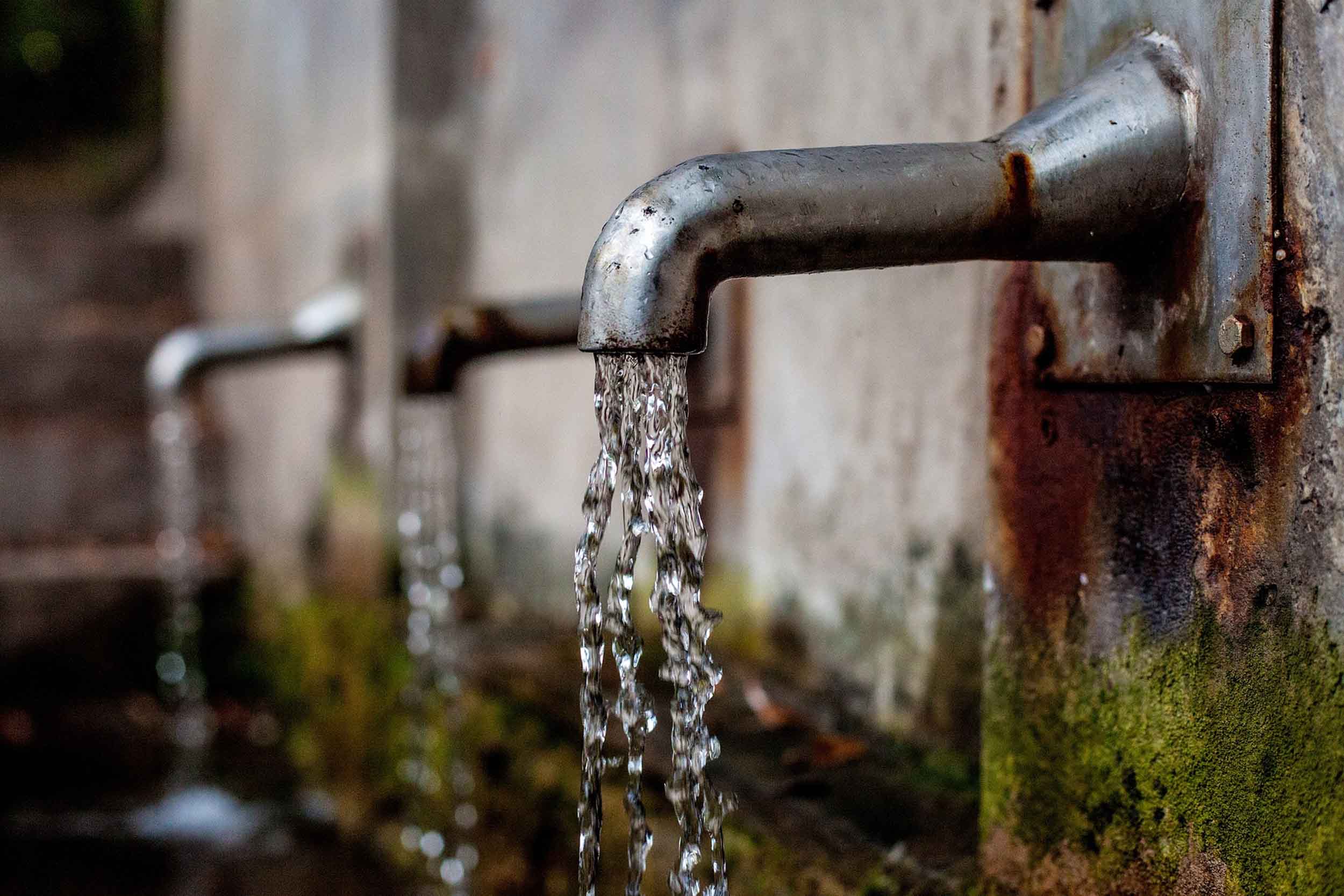 Stock image of a rustic outdoor water faucet with water coming out.