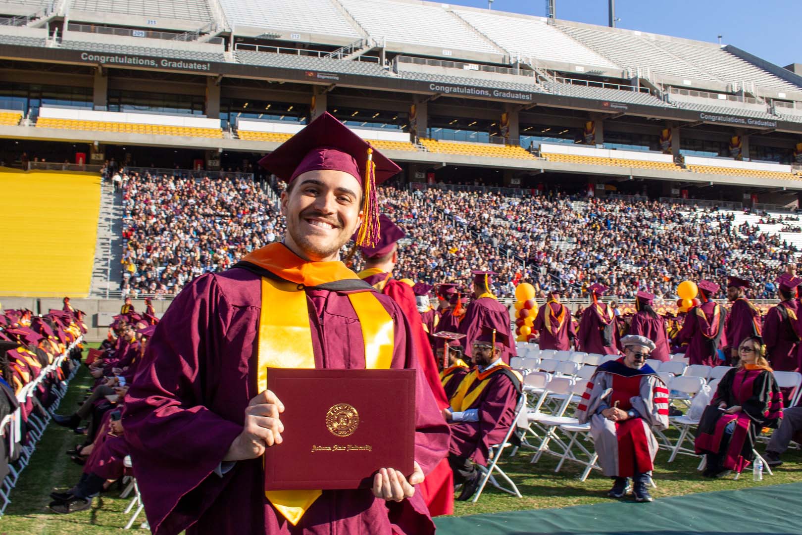 A master's graduate holds his diploma on the field at Sun Devil Stadium during the Fulton Schools Convocation ceremony.