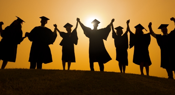 Silhouetted students standing in a line with graduation caps on in front of a golden sunset