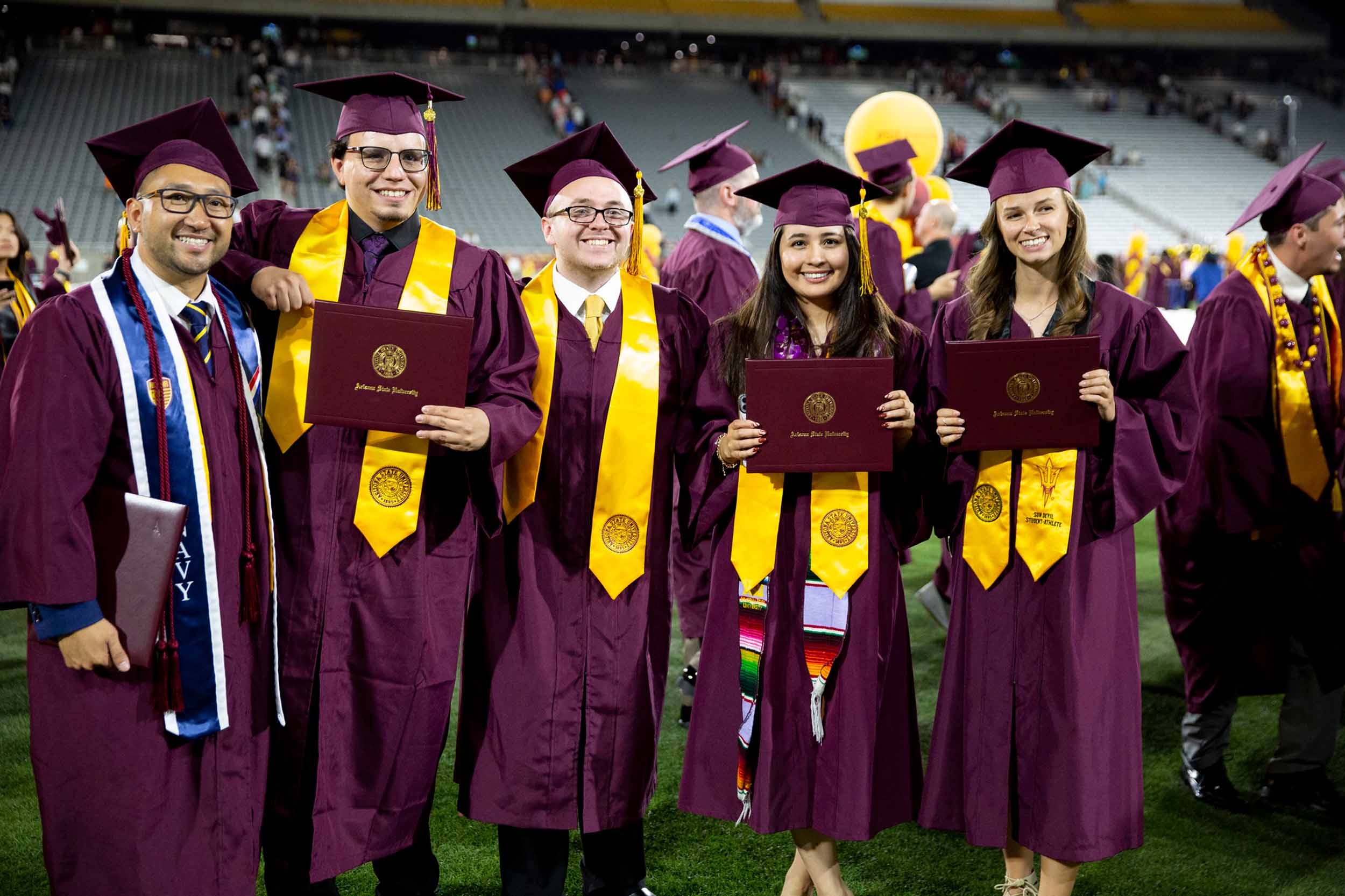 A group of 5 graduates stand together for the camera after a Fulton Schools Convocation ceremony in Sun Devil Stadium.