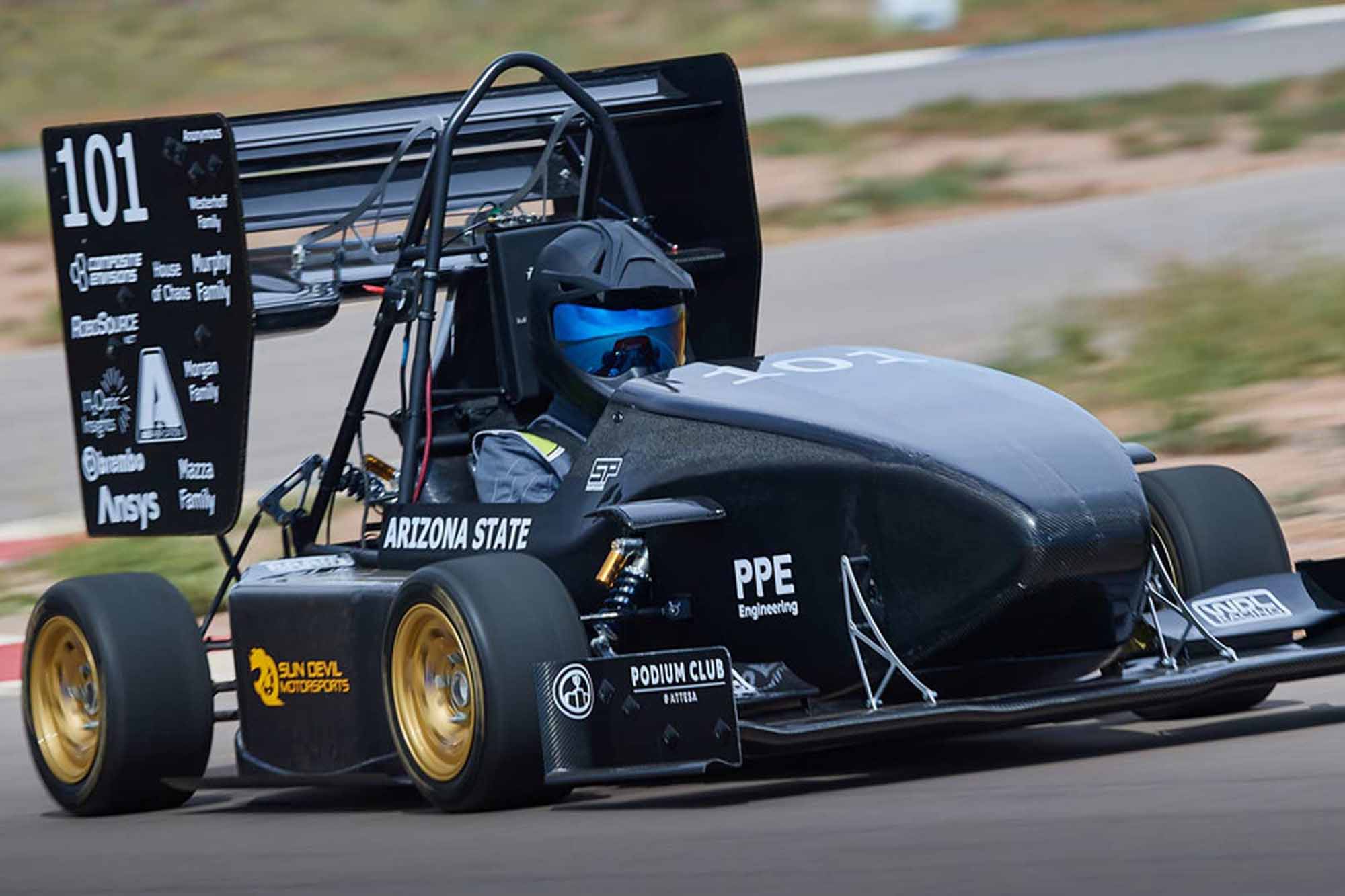 A driver is driving the latest Sun Devil Motorsports race car, the SDM23, on a racetrack, the blurred desert background showing the high speed of travel.