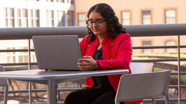 An Arizona State University online computer science bachelor's student sits outside at a table working on her laptop computer.