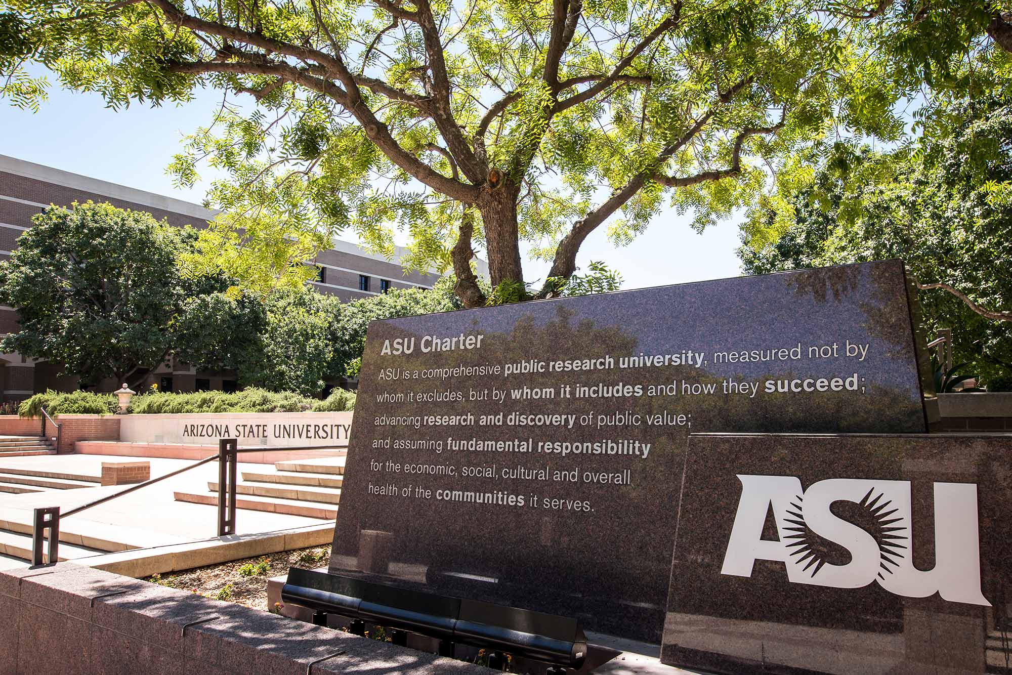 A scene from a sunny day on the ASU West campus, where you can see a large marble monument displaying an engraving of the ASU Charter