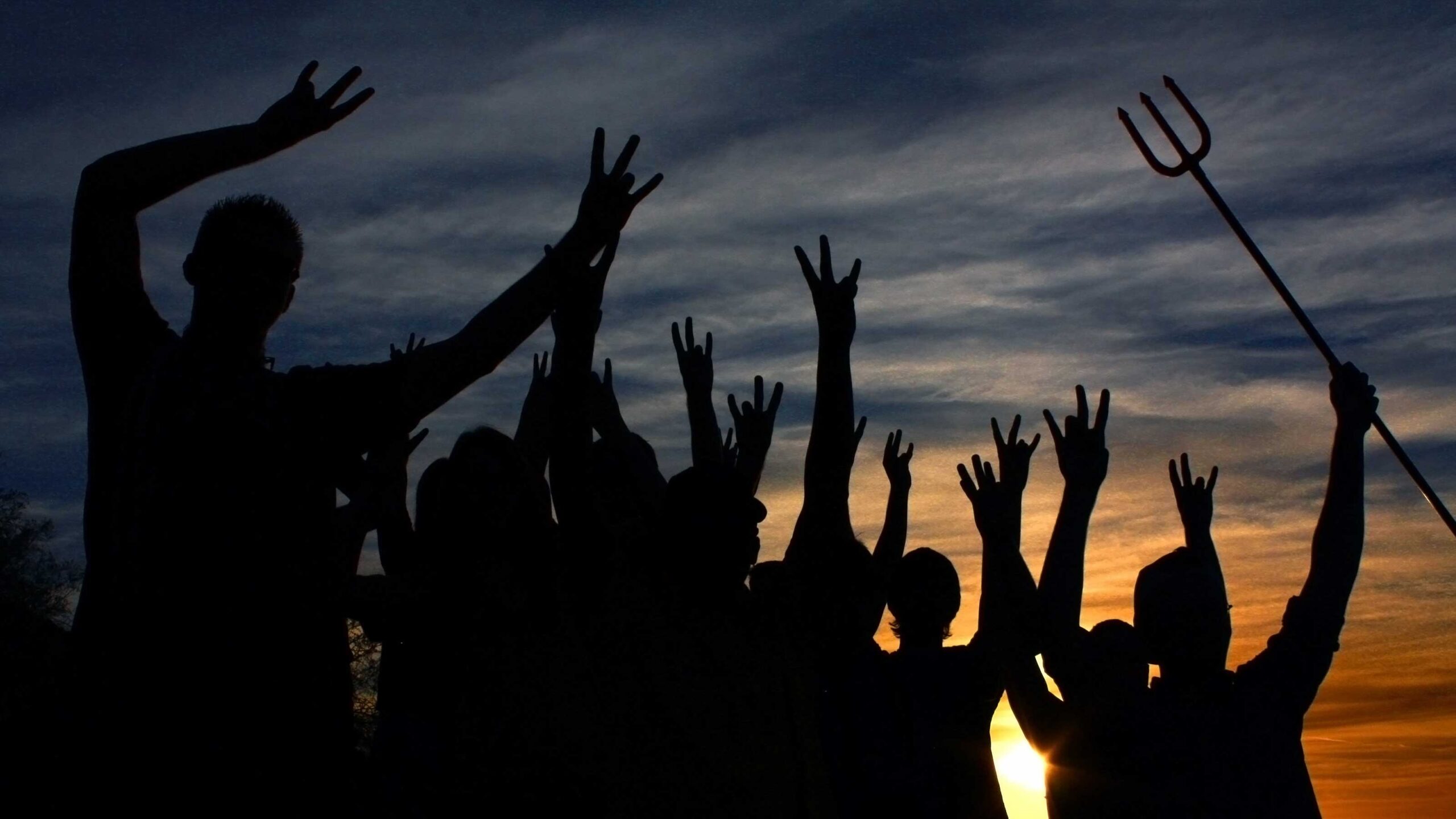 A group of students silhouetted against a sunset throws up the fork hand signal.