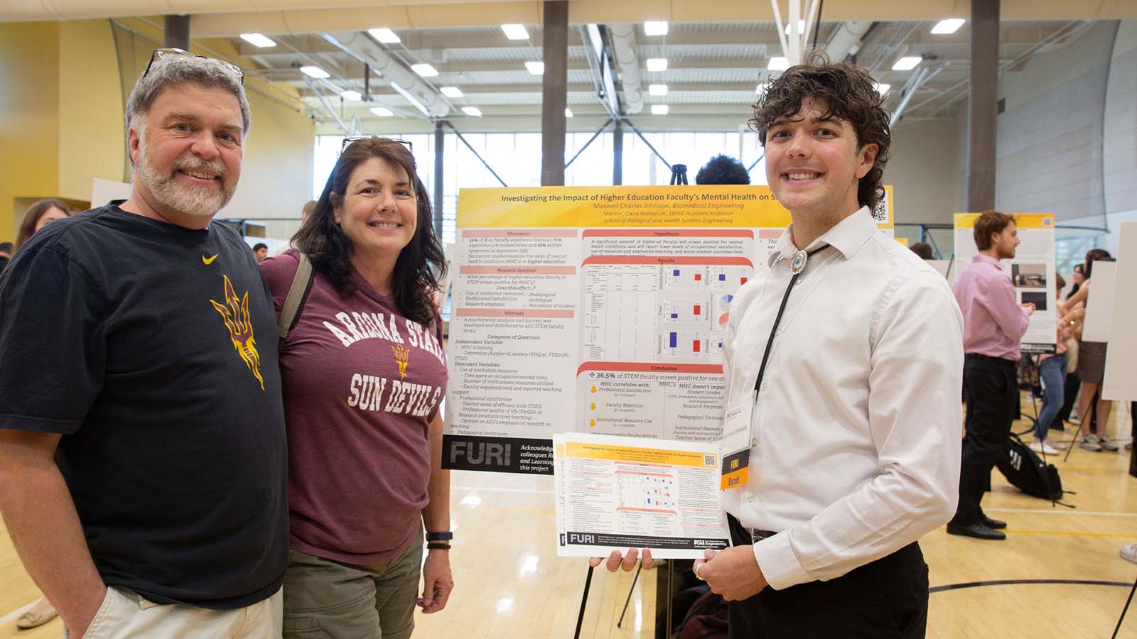 An ASU Engineering student and his parents stand together at his student research presentation poster at a student research showcase event.