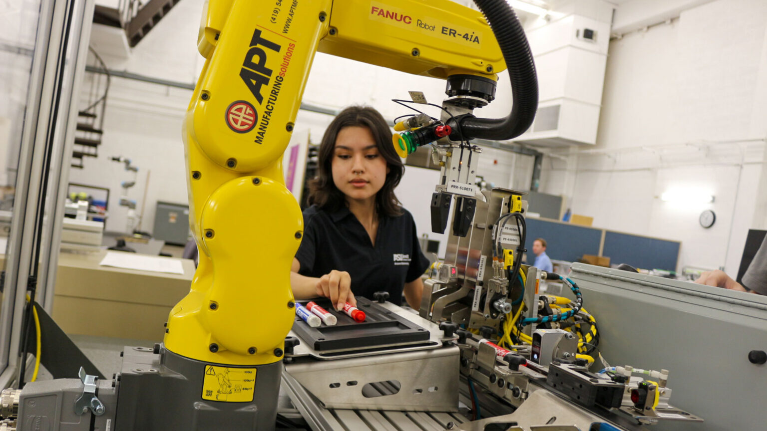 A woman stands in a manufacturing lab working with a manufacturing robot
