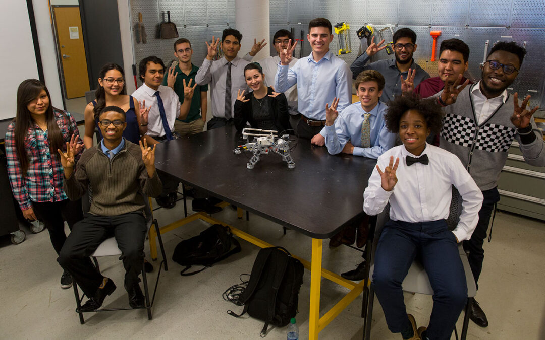 A group of students poses around a robot.